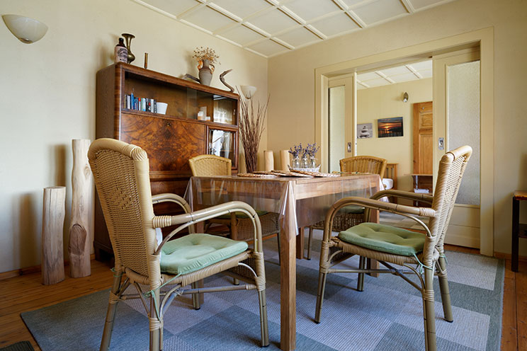 Holzesstisch mit vier Armlehnstühlen und dunkler Holzschrank, natürliche Dekoration mit Lavendel und Treibholz, helle lehmverputzte Wände. Aufgearbeiteter Dielenboden.  